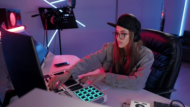Woman artist plays on synthesizer in recording studio. Musician sits in chair at the table with music studio setup.