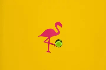 Fotobehang pink flamingo kicks a green ball, creative summer design on a yellow background © Stefan