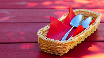 Two metal spoons lie on red paper napkins in a cutlery basket on a red wooden table. The idea of the beginning of the meal, bon appetit - obrazy, fototapety, plakaty
