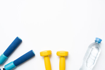 Flat lay of fitness equipment on white background. Top view of jump rope, dumbbells and bottle of water for home workout. Fitness objects on white background with copy space