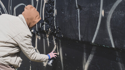 guy in a hood and black glasses writes graffiti
