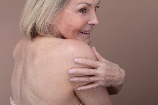 Studio shot of shirtless senior woman touching shoulder