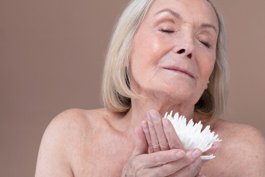 Studio shot of shirtless senior woman with eyes closed holding white flower