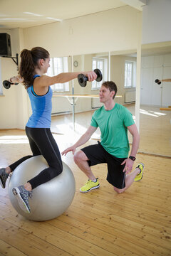Gym workout with personal trainer using fitness ball