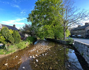 Fototapeta na wymiar Looking over, Malham Beck, with trees, and old stone cottages, in the centre of the Yorkshire Dales village of, Malham, Skipton, UK