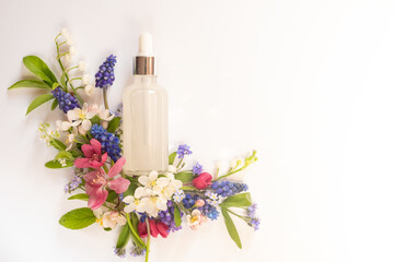 Obraz na płótnie Canvas Cosmetic glass transparent bottle with dropper for hyaluronic acid among different wildflowers on a white background. Beautiful light reflections.