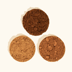 Natural and alkalized cocoa. Comparison of dutch process cocoa with natural cocoa powder. Three piles of texture cocoa powder of different colors on a beige background. Top view.