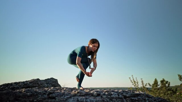 Woman practicing in Garudasana - eagle pose, yoga on high mountain above water. Flexibility workout at nature background. Strong lady strengthening neck and back