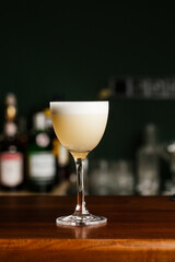 Pisco sour cocktail - whiskey with lime, egg white, sugar syrup in glass on dark blurred background. Space for text