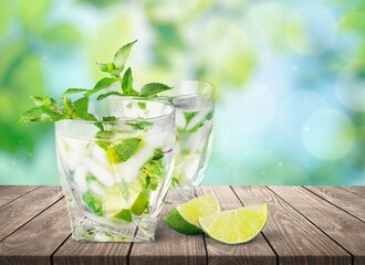 Fresh lemonade drink or alcoholic cocktail with ice, mint and lemon slices on blur background.