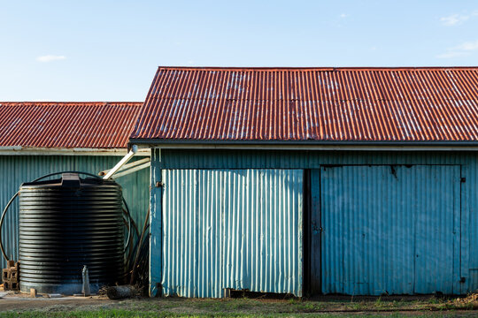 Corrugated iron farm shed painted blue, with red roof, and water tank.