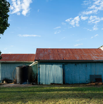 Corrugated iron farm shed painted blue, with red roof, and water tank.