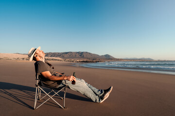 man in camping chair on the beach with a soft drink or beer relaxing at sunset