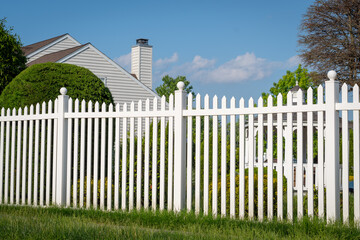 White vinyl fence in a cottage village tall thuja bushes behind the fence fencing of private...
