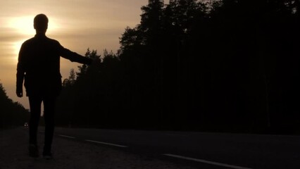 Silhouette of young adult hitchhiking during sunset time. Pick me up concept