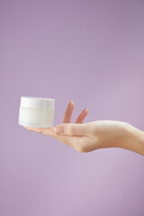 Front view of hand model holding cosmetic jar in purple background for cosmetic advertising