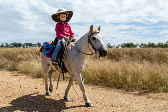 A six year old boy riding his white pony on a dirt road.
