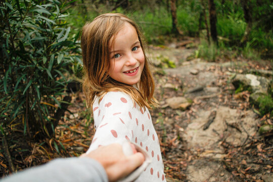 Young girl smiling in the wild holding parents hand on an adventure