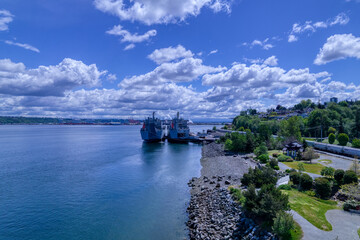 Obraz premium Two ships docked on the rocky shores of Puget Sound in Tacoma, Washington under a blue cloud filled sky.