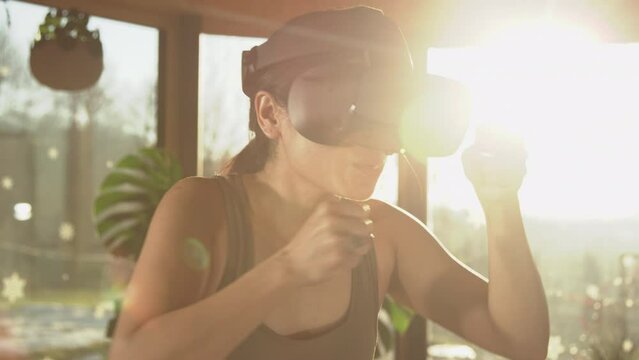 CLOSE UP: Sporty Asian woman having fun boxing at home using modern VR goggles. Sports and virtual reality concept. Asian lady doing boxing exercises at home with futuristic technology virtual device.