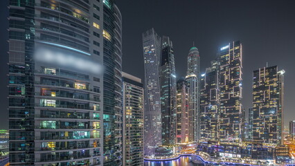 Dubai marina tallest skyscrapers and yachts in harbor aerial night timelapse.