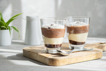 Delicious three-layer mousse, vanilla, chocolate, creme brulee dessert in a glass in the bright rays of the sun. 