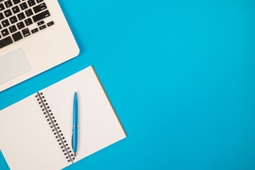 Top view photo of pen with notepad and laptop on isolated blue background