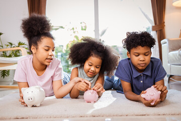 African American kids putting a coin into a piggy bank in a living room at home