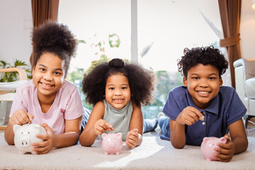 Portrait of African American kids saving money in a piggy bank in living room at home