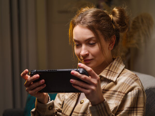 A girl with a gamepad plays a video game online with friends. Rejoices to win, emotionally reacts. Communications, new digital technologies, youth culture, competitions, tournaments, battles.