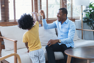 Portrait of African American father and son having fun playing with toy airplane in living room at...