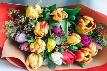 A colorful bouquet of spring tulips in bright red wrapping paper lies on the table.