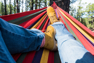 Close up of pair of trekker legs having relax outdoor leisure activity laying on a colorful hammock...