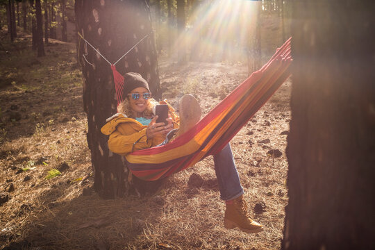 Cheerful portrait of beautiful woman enjoy relax at the mountain lay down on hammock on nature forest woods outdoors park and smiling to cellular phone - roaming connection and smart working job