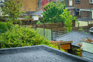 Deszczowy dzień, krople deszczu uderzające o dach. Ogródki w domach jednorodzinnych podczas deszczu, rośliny i drzewa.
