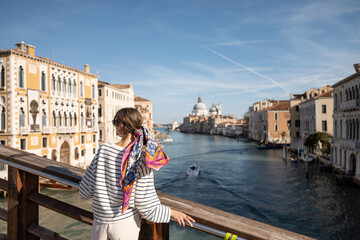 Fototapeta na wymiar Young woman enjoying beautiful view on Grand Canal from Academy bridge in Venice. Idea of spending summer time and travel in Italy. Caucasian female wearing striped vest and colorful shawl