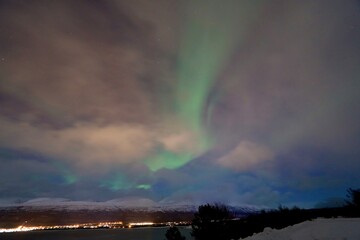 northern lights in norway near tromso. green lights and blue sky with clouds.
