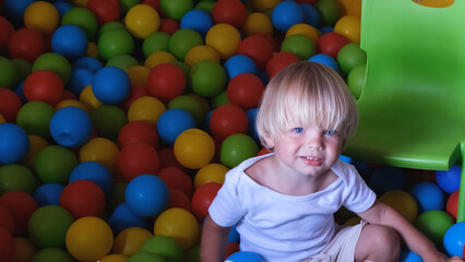 Fototapeta na wymiar Happy playful little boy 2-3 years old in dry pool with colorful plastic balls