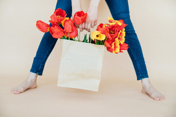 Women's hands hold a bouquet of red tulips in a paper bag on a beige background. Valentine's Day,...