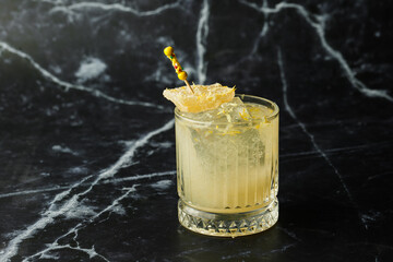 Alcoholic Scotch Whiskey Penicillin Drink Cocktail with Lemon, Honey syrup and Candied Ginger. Cocktail glass on black background