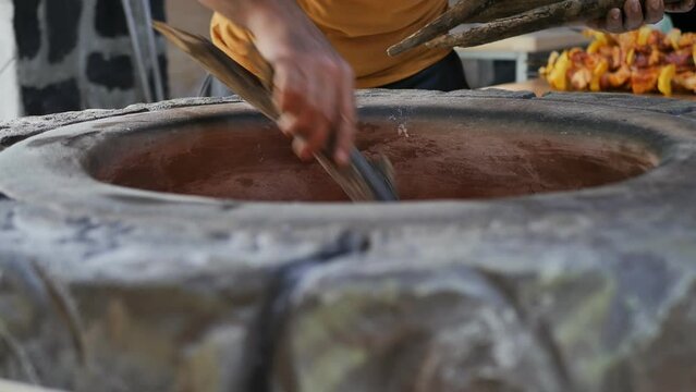 a man baker kindles a stone tonir by laying firewood with his hands. National bakery building made of stone for cooking traditional bread and khorovats.
