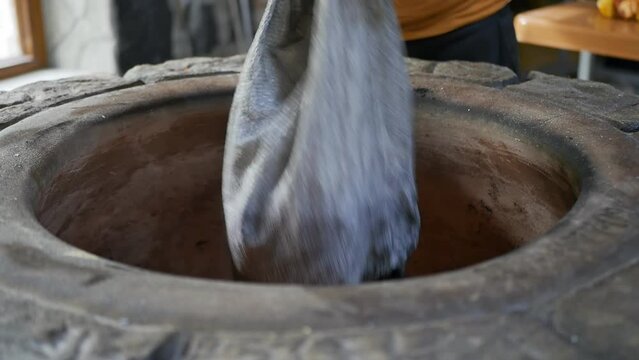 An Armenian baker pours coal from a bag into a stone tonir with fire inside. Filling charcoal into the tandoor for baking bread and Yerevan khorovats. National bakery tone of Transcaucasia