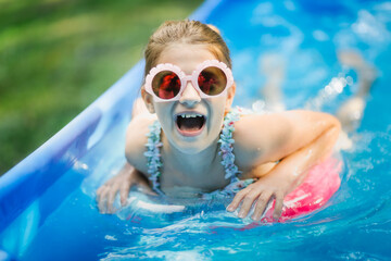 Stylish preteen kid girl swims with circle in pool. Funny child in pink glasses with shells and...