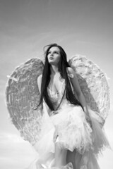 Sweety angel, woman with wings. Sensual female angel posing over a cloudy sky with feathers.