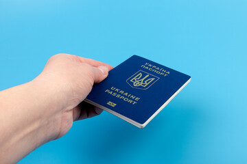 Passport of a citizen of Ukraine in a female hand on a blue background, close-up. Inscription in Ukrainian Ukraine Passport