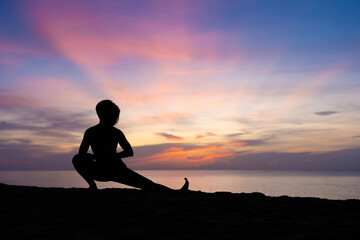 Silhouette of beautiful woman practicing yoga asana on the beach with sunrise on twilight blue vibrant sky and calm sea in background. Skandasana, Side lunge, Stretching, Power concept, Meditation.