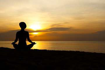 Silhouette of beautiful woman sitting cross legged in easy seat pose on the beach with sunrise in background, relaxing deep breathing meditating body and mind. Yoga poster, Backdrop, Balancing concept