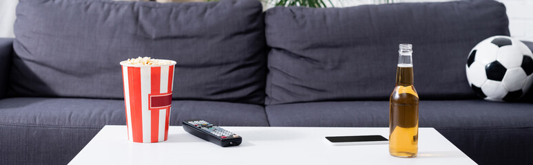 sofa with soccer ball near table with bucket of popcorn, beer, tv remote controller and smartphone, banner.