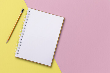 White notebook with pencils placed on pink and yellow background.