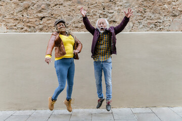 portrait of happy multiracial senior couple jumping in the city- retired concept -